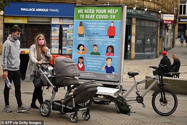 A couple wearing a protective face masks in Halifax pass a promotion funded by Calderdale Council - an ad bike display advising people to keep their distance and book a test if they have symptoms