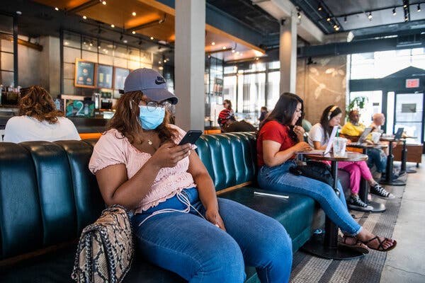 Masked and unmasked people in a Starbucks in Manhattan on Tuesday. The C.D.C. now recommends that even vaccinated people wear masks in communities where the virus is surging. 